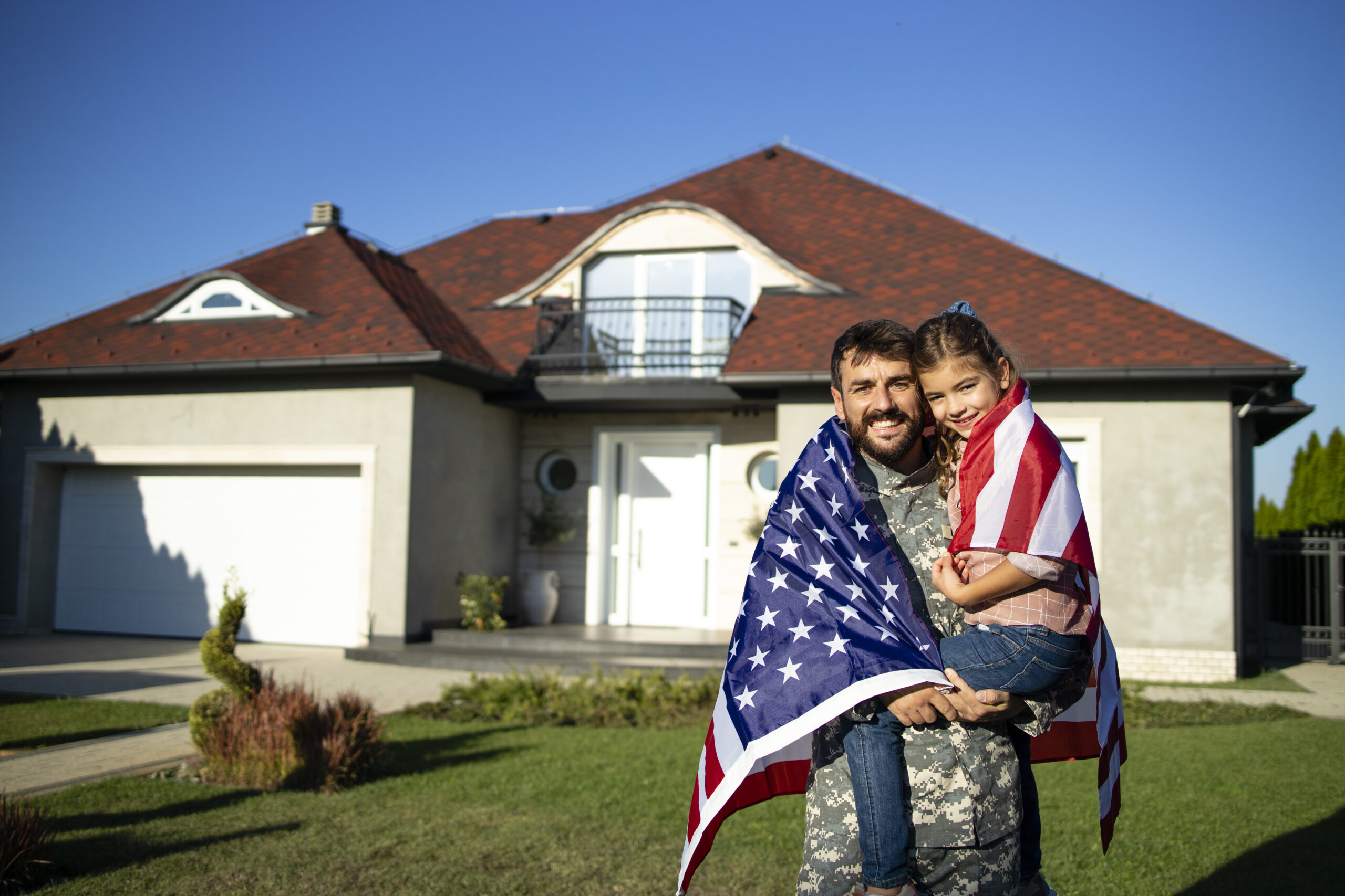 Portrait of father soldier on military leave holding his lovely daughter in front of their house.