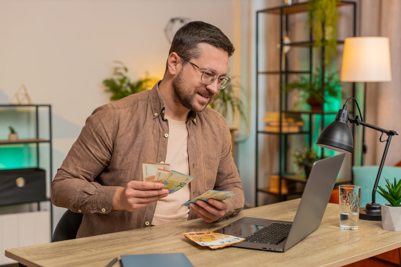 Rich happy Caucasian man counting money euro cash using laptop calculate domestic bills at home