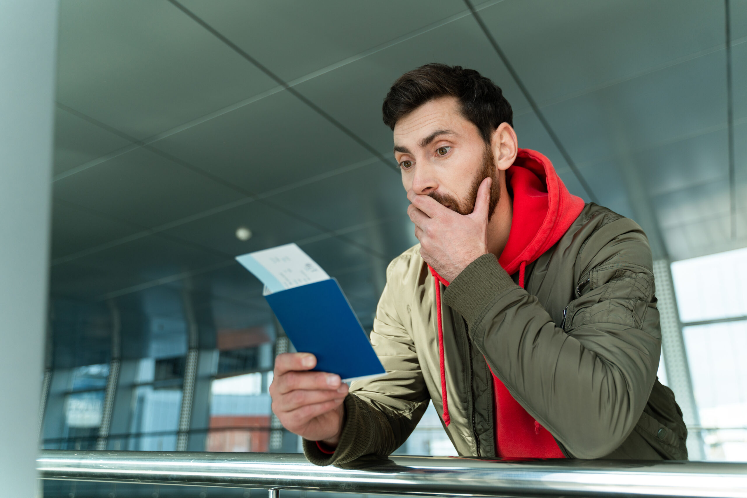 Waist up portrait of shocked man standing at the airport and looking at his passport with surprised expression while waiting for departure. Technologies and people concept